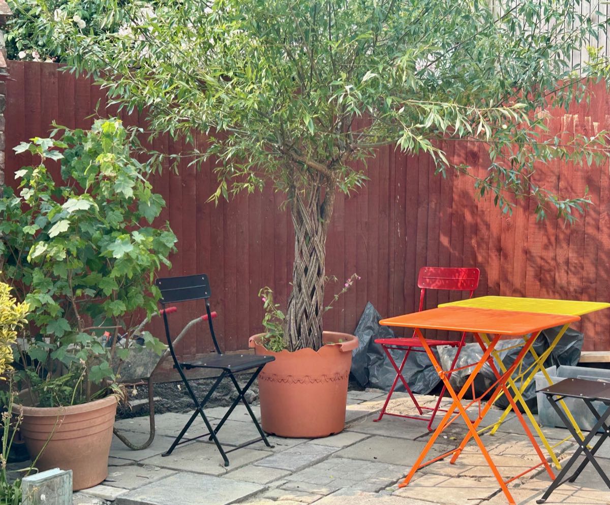 The courtyard: a small tree in a pot, bistro tables and folding chairs against a red fence.