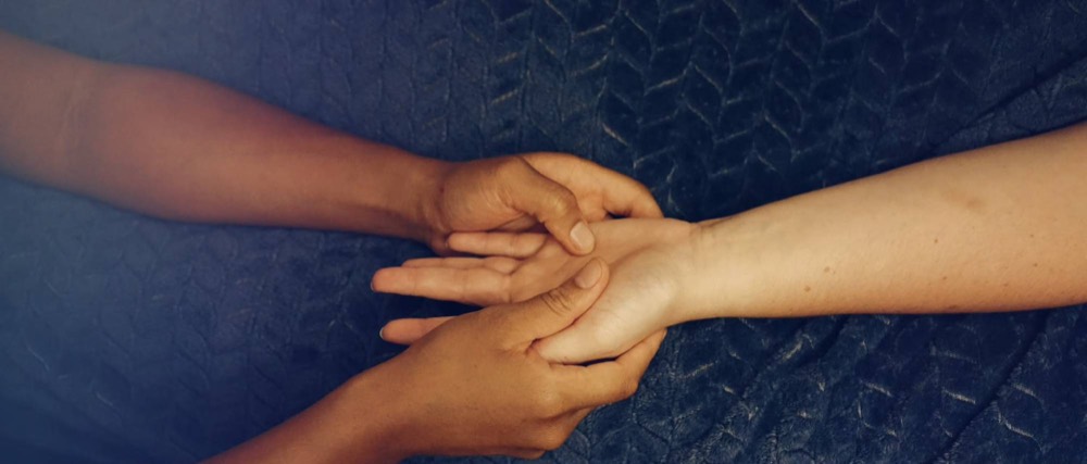 A hand massage in progress, the client's forearm resting on a dark blue cover.