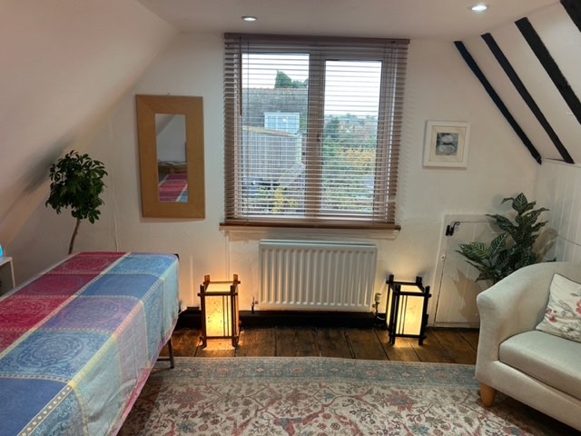 The Loft: a therapy bed under a sloping ceiling, with lanterns, plants and a window over the rooftops.